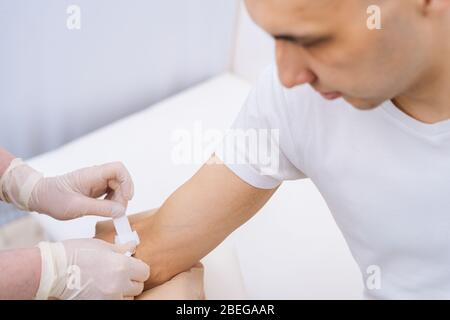 Krankenschwester in Gummischutzhandschuhen, die einen Klebeverband auf den Arm des jungen Mannes legt Stockfoto