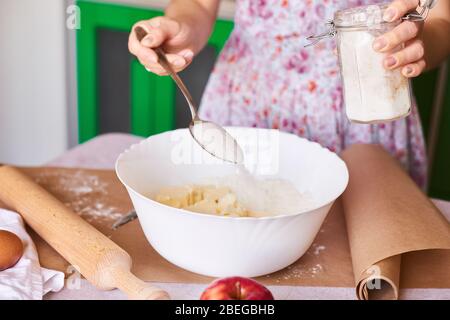 Frau legte Zutaten für Apfelkuchen in große weiße Schüssel. Teig in der Küche vorbereiten Stockfoto