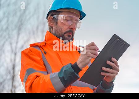 Forsttechniker sammelt Daten in Wald und schreibt Notizen auf Notizblock in der Zwischenablage Stockfoto