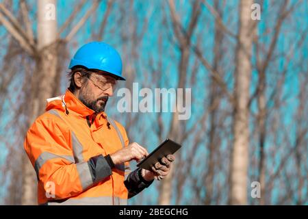 Forsttechniker, der einen digitalen Tablet-Computer in der Waldstruktur verwendet, um während der Entwaldung Daten zu erfassen Stockfoto