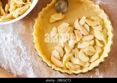 Frau fügt in Scheiben geschnittene Äpfel zu Apfelkuchen. Frau Hände arbeiten einen Kuchenteig in einem Tablett, auf einem Küchentisch, umgeben von Kürbiskuchen Zutaten. Tradition Stockfoto