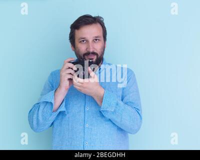 Porträt des männlichen Fotografen in blauem Hemd mit alten analogen slr-Art-Kamera, während sie vor cyanfarbenem Hintergrund stehen Stockfoto