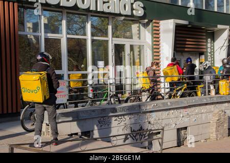 Kiew. Ukraine - 12. April 2020: Kuriere und Lieferdienste Glovo in der Warteschlange in der Nähe des McDonald's. Ukraine stoppt Bars, Restaurants und Einkaufsmöglichkeiten ce Stockfoto