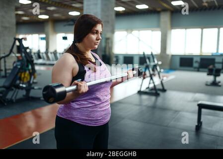 Übergewichtige Frau mit Hanteln auf brench im Fitnessstudio Stockfoto