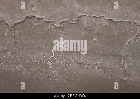 Sandiger Boden des getrockneten Reservoirs mit den Rissen und den Salzkristallen. Stockfoto