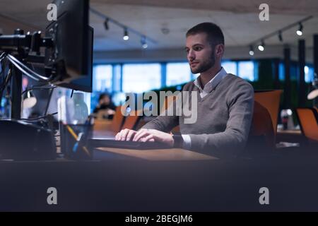 Junger Geschäftsmann, der an einem Computer im gemeinsamen Arbeitsraum arbeitet. Ein feiger Prozess, ein Geschäftsmann, der in einem modernen Büro arbeitet. Stockfoto