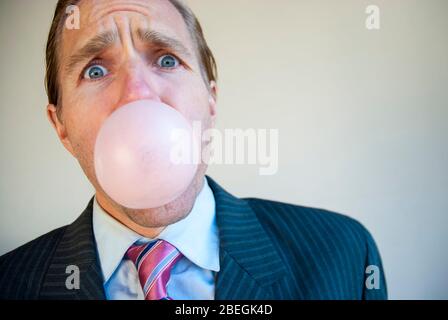 Besorgt Geschäftsmann Blick auf die Kamera weht eine rosa Blase aus Gummi immer bereit zu platzen Stockfoto