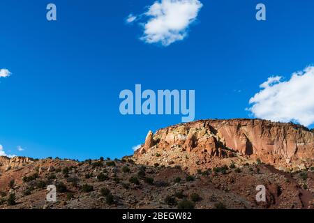 Eine bunte Wüste mesa mit Sandstein Felsformationen und Klippen unter einem riesigen blauen Himmel durch Sonnenlicht durch Brüche in flauschigen weißen Wolken i beleuchtet