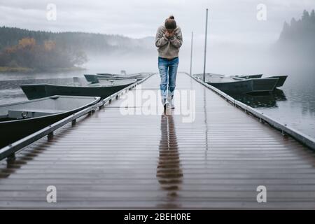 Junge Frau schaut hinunter, während sie über das nasse Dock im Nebel geht Stockfoto