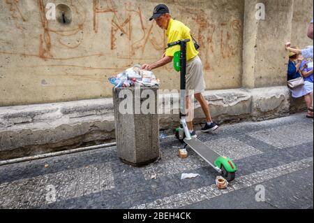 PRAG - 20. JULI 2019: Ein Mann, der Müll in einen überlaufenden Mülleimer neben einem Elektromoped zum Mieten legt, auf einer Straße in Prag Stockfoto