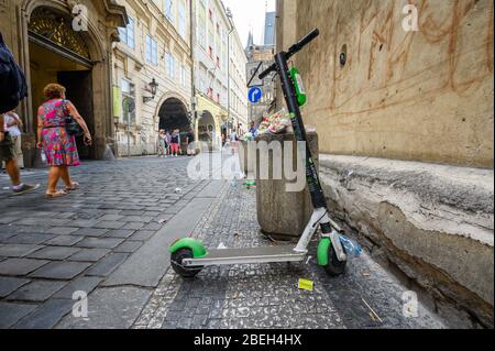 PRAG - 20. JULI 2019: Ein Elektromoped zum Mieten, der neben überlaufenden Mülltonnen mit Müll auf einer alten Kopfsteinpflasterstraße in Prag geparkt ist Stockfoto