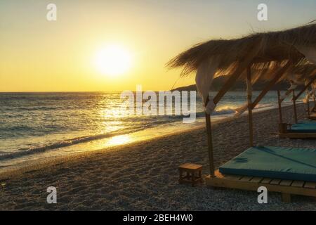 Sonnenuntergang am Strand Livadi bei Himare, Albanien, Europa. Strandhaus mit Sonnenliegen am Strand Ionische Küste. Stockfoto