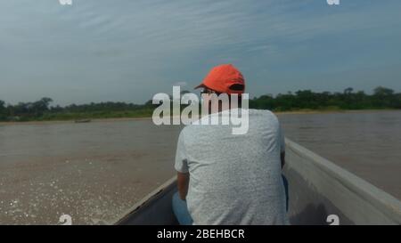 Schwarzer Mann mit Mütze segelt auf einem Holzboot im Aguarico Fluss an einem sonnigen Morgen Stockfoto