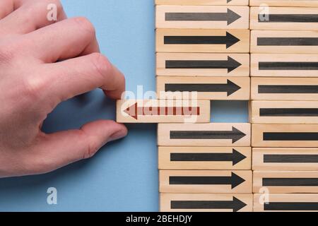 Alternative Business Development Konzept - Hand hält Holzwürfel mit rotem Pfeil auf blauem Hintergrund. Nahaufnahme. Stockfoto
