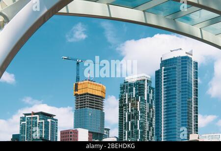 Moderne Hochhäuser mit Hochhäusern, die mit Kräne umrahmt sind, die von einem Stahl- und Glasbogen entlang der Uferpromenade von Seattle, Washington, umgeben sind Stockfoto