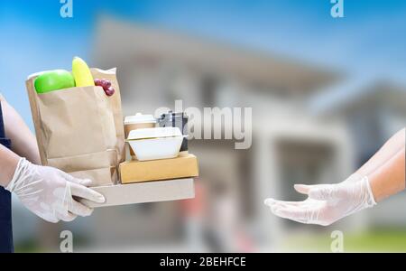 Der Lieferer hält Lebensmittelboxen und Kaffee mit Gummihandschuhen. Online-Shopping und kostenlose Lieferung zu Hause. Soziale Distanzierung und Aufenthalt zu Hause bleiben Sie sicher. Stockfoto