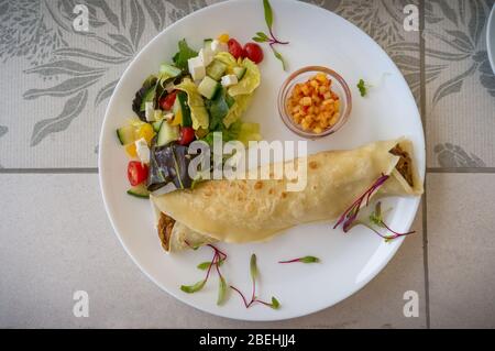 Draufsicht auf französisch Crepe mit Schweinefleisch und Salat auf der Seite mit Mais Salsa und Salat Grüns als Beilage. Leichte Mahlzeit, Snack auf weißem Teller. Stockfoto