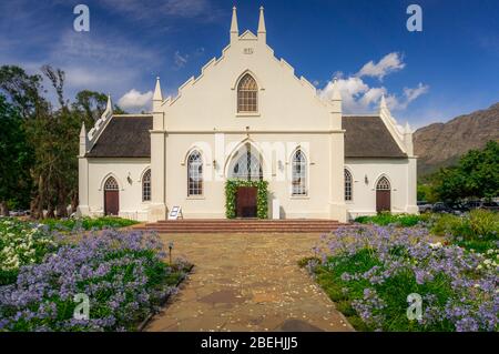 Historische weiß getünchte holländische Reformierte Kirche an der Hauptstraße in Franschhoek, im Franschhoek Tal mit Berg im Hintergrund Stockfoto