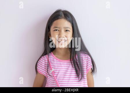 Asiatisches kleines Mädchen lächelt hell. Kinder, die rosafarbene weiße Kleider und langes schwarzes Haar tragen. Das Kind blickt nach vorne und lächelt glücklich. Porträts Stockfoto