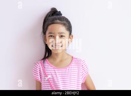 Porträt eines kleinen asiatischen Mädchens mit einem rosa-weiß gestreiften Kleid. Das Kind Band schwarze Haare zusammen und lächelte glücklich. Stockfoto