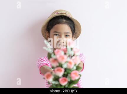Porträt eines kleinen asiatischen Mädchens mit einem rosa-weiß gestreiften Kleid. Das Kind trägt einen Hut und hält Rosenblumen mit Lächeln und glücklich. Wählen Sie Stockfoto