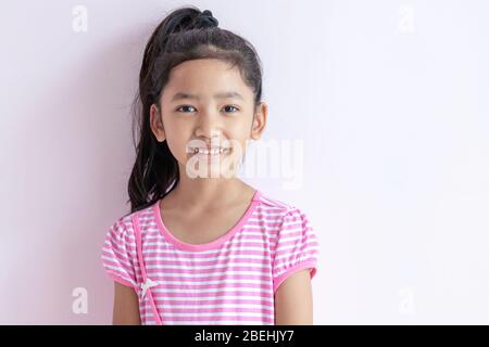 Porträt eines kleinen asiatischen Mädchens mit einem rosa-weiß gestreiften Kleid. Das Kind mit schwarzen Haaren lächelt hell.