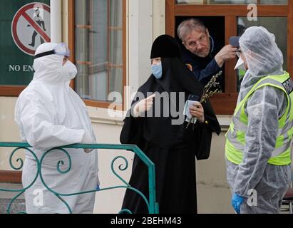 Kiew, Ukraine. April 2020. Eine Nonne mit Gesichtsmaske spricht mit einem Sanitäter am geschlossenen Eingang des Kiewer Pechersker Lavras in Kiew.Kiewer Pechersker Lavras Abschaltung zur Quarantäne als das COVID-19 Coronavirus-Brutstätte. Am 13. April 2020 erklärte der Bürgermeister von Kiew, Witaliy Klitschko, dass die COVID-19 bestätigte Fälle im Kiewer Pechersk Lavra auf mehr als 90 angestiegen sind, darunter 63 Fälle, die am vergangenen Tag bestätigt wurden. Die Kiew Pechersk Lavra, die eine der wichtigsten orthodoxen Heiligtümer, seit ihrer Gründung als Höhlenkloster im Jahr 1051, die Lavra ist ein herausragendes Zentrum der östlichen orthodoxen Christianit Stockfoto