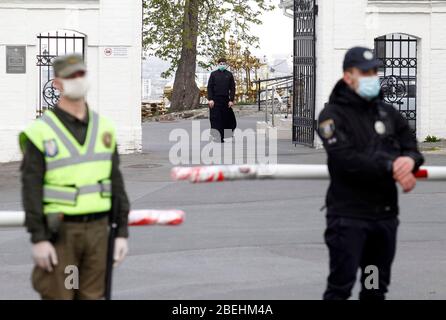 Kiew, Ukraine. April 2020. Ukrainisch-orthodoxer Pfarrer (C) geht in Richtung der Nationalgarde Soldaten blockieren die Straße zum Eingang der Kiew Pechersk Lavra.Kiew Pechersk Lavra Abschaltung für Quarantäne als die COVID-19 Coronavirus Brutstätte. Am 13. April 2020 erklärte der Bürgermeister von Kiew, Witaliy Klitschko, dass die COVID-19 bestätigte Fälle im Kiewer Pechersk Lavra auf mehr als 90 angestiegen sind, darunter 63 Fälle, die am vergangenen Tag bestätigt wurden. Die Kiew Pechersk Lavra, die eine der wichtigsten orthodoxen Heiligtümer, seit ihrer Gründung als Höhlenkloster im Jahr 1051 ist die Lavra ist ein herausragendes ce Stockfoto