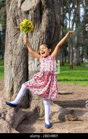 Kleines Mädchen im Kleid feiert im Park mit einem Blumenstrauß in der Hand Stockfoto