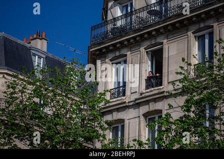 Paris, Frankreich. April 2020. Eine Frau genießt den Sonnenschein an ihrem Fenster in Paris, Frankreich, 13. April 2020. Frankreich werde bis Mai 11 unter einer landesweiten Lockdown-Regierung stehen, um die Ausbreitung von COVID-19 einzudämmen und seine Auswirkungen auf die heimischen Gesundheitseinrichtungen zu verringern, sagte Präsident Emmanuel Macron am Montagabend. Kredit: Aurelien Morissard/Xinhua/Alamy Live News Stockfoto