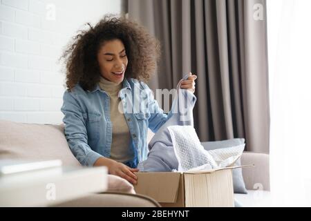 Überrascht afrikanischen jungen Frau Shopper Auspacken Mode Lieferbox zu Hause. Stockfoto