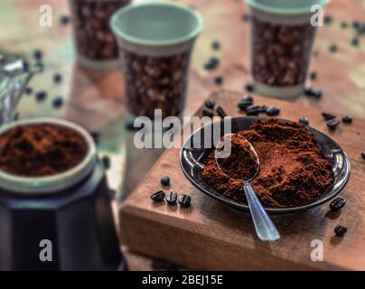 Ein Teller mit gemahlenem Kaffee und einem Löffel auf einem Tisch, umgeben von Kaffee Stockfoto