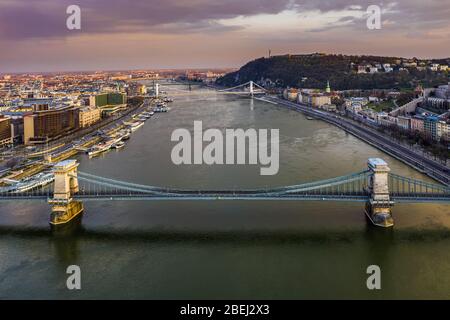 Budapest, Ungarn - Luftaufnahme der völlig leeren Szechenyi Kettenbrücke bei Sonnenuntergang mit Elisabeth Brücke, Zitadelle und buntem Himmel im Hintergrund. Kein tr Stockfoto