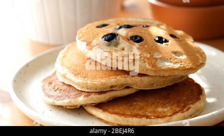 Große amerikanische Pfannkuchen mit Heidelbeeren auf dem Teller mit natürlichem Morgenlicht. Süßes Frühstück Stockfoto