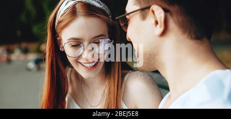 Rothaarige kaukasische Frau mit Sommersprossen und Brillen, die mit ihrem Geliebten auf der Bank im Park lachend ist Stockfoto