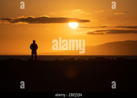 Los Angeles, USA. April 2020. Eine Person steht am Strand von Venice Beach und beobachtet den Sonnenuntergang. Bild: Maximilian Haupt/dpa/Alamy Live News Stockfoto