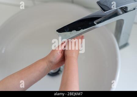 Mädchen waschen Hände unter einem modernen Wasserhahn und sinken während der COVID-19 Pandemie 2020 Stockfoto