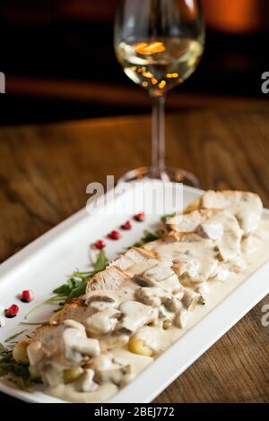 Hühnerfleisch auf geriebenem Gnocchi in Sahnesauce aus Pilzen und geräuchertem Käse auf dem Tisch mit Glas Weißwein Stockfoto