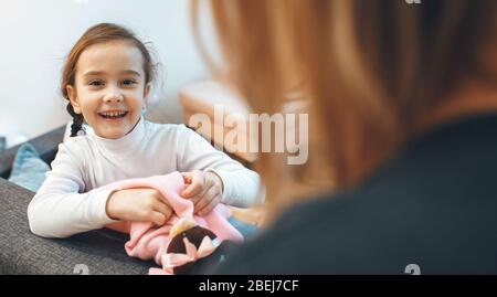 Fröhliches Mädchen und ihre Mutter spielen mit einem Teddybären im Wohnzimmer Stockfoto