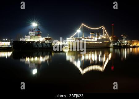 Turku, Finnland - 21. März 2020: Schlepper und altes Hotelboot liegen am Aura-Fluss in Turku, Finnland, an einer stimmungsvollen Frühlingsnacht. Aufnahme mit langer Belichtung. Stockfoto