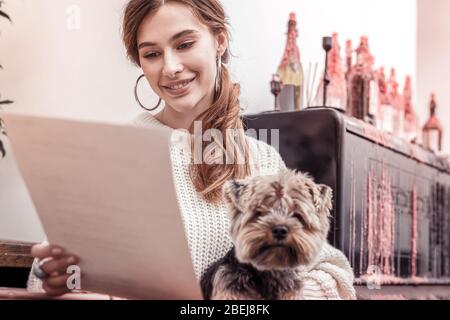 Nahaufnahme einer hübschen Frau mit ihrem flauschigen Haustier im Café, die ein Menü liest Stockfoto