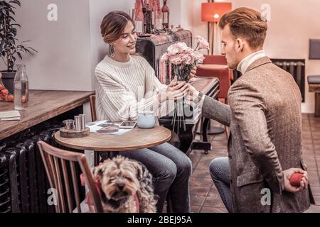 Szene im Café. Mann, der auf dem Knie steht, verschenkt Blumen an Freundin, die an einem schönen Tag einen Heiratsantrag machen möchte Stockfoto