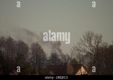 Schwarzer Rauch, der aus dem Kamin des Hauses ausströmt, der auf die Verbrennung von Müll hinweist. Stockfoto