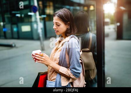 Fröhliche junge Frau, die nach dem Einkaufen in der Stadt Kaffee trinkt und mit Taschen spazieren geht. Stockfoto