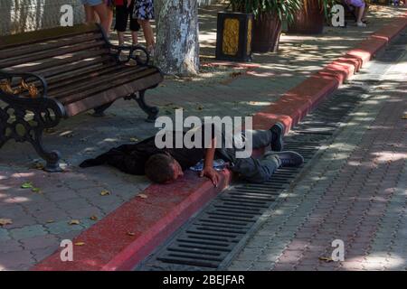 Kerch, Russland - 13. August 2019: Ein betrunkener Mann schläft an einem Sommertag auf dem Bürgersteig im Stadtzentrum Stockfoto