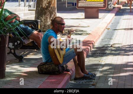 Kerch, Russland - 13. August 2019: Ein Straßenmusiker spielt Gitarre und singt während er an einem Sommertag auf dem Bürgersteig sitzt Stockfoto