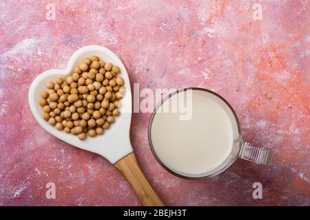 Von oben gesehen, auf rustikalem Hintergrund, ein Glas mit Sojamilch und Sojabohnen im herzförmigen Löffel. Stockfoto