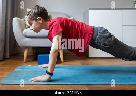 Kleiner Junge auf Yoga-Matte zu Hause hält Plank Pose. Körperliche Aktivität des Kindes zu Hause in Quarantäne Stockfoto