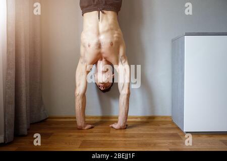 Junger Mann, der zu Hause im Handstand steht. Körperliche Ausbildung zu Hause Isolation während der Quarantäne Stockfoto