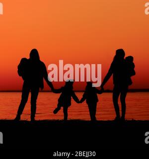 Zwei Mutter und kleine Tochter genießen die Sonne am Fluss im Sommer bei Sonnenuntergang. Im Freien Stockfoto
